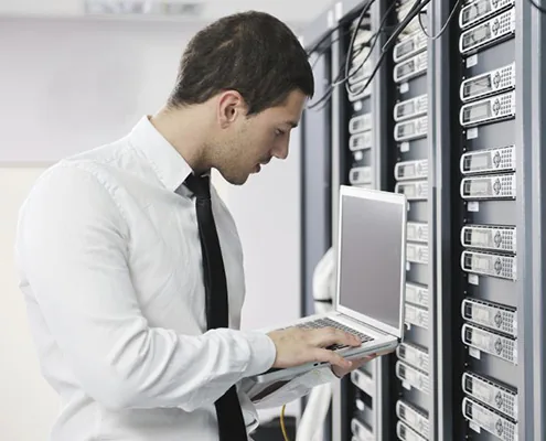 Tecnico al lavoro con un portatile accanto ai server in sala macchine